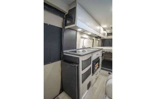 An RV rental interior with a bright kitchen, featuring a sink, microwave, and refrigerator next to the bed.