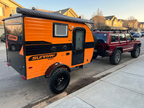 Orange Sunray Sport teardrop trailer, great for rv rental, hitched to a red off-road SUV. Ready for adventure!