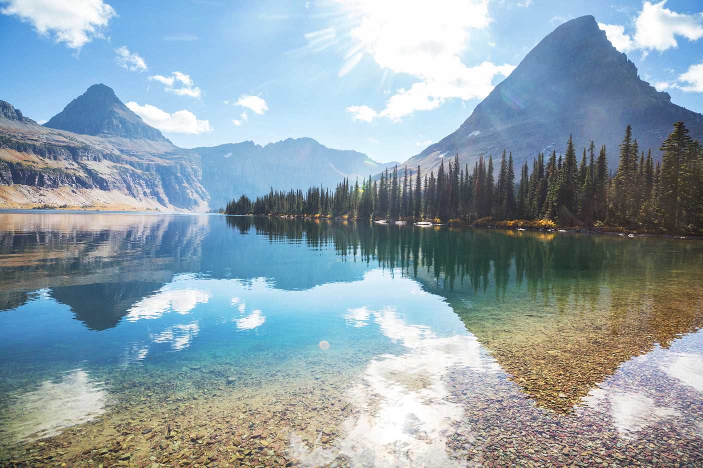 Serene mountain lake reflecting peaks & clear sky, lined by evergreens. Ideal RV rental destination for tranquil nature adventures.