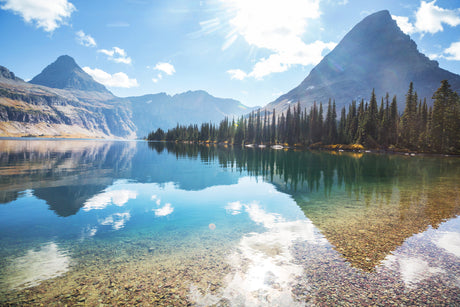 Serene mountain lake reflecting peaks & clear sky, lined by evergreens. Ideal RV rental destination for tranquil nature adventures.