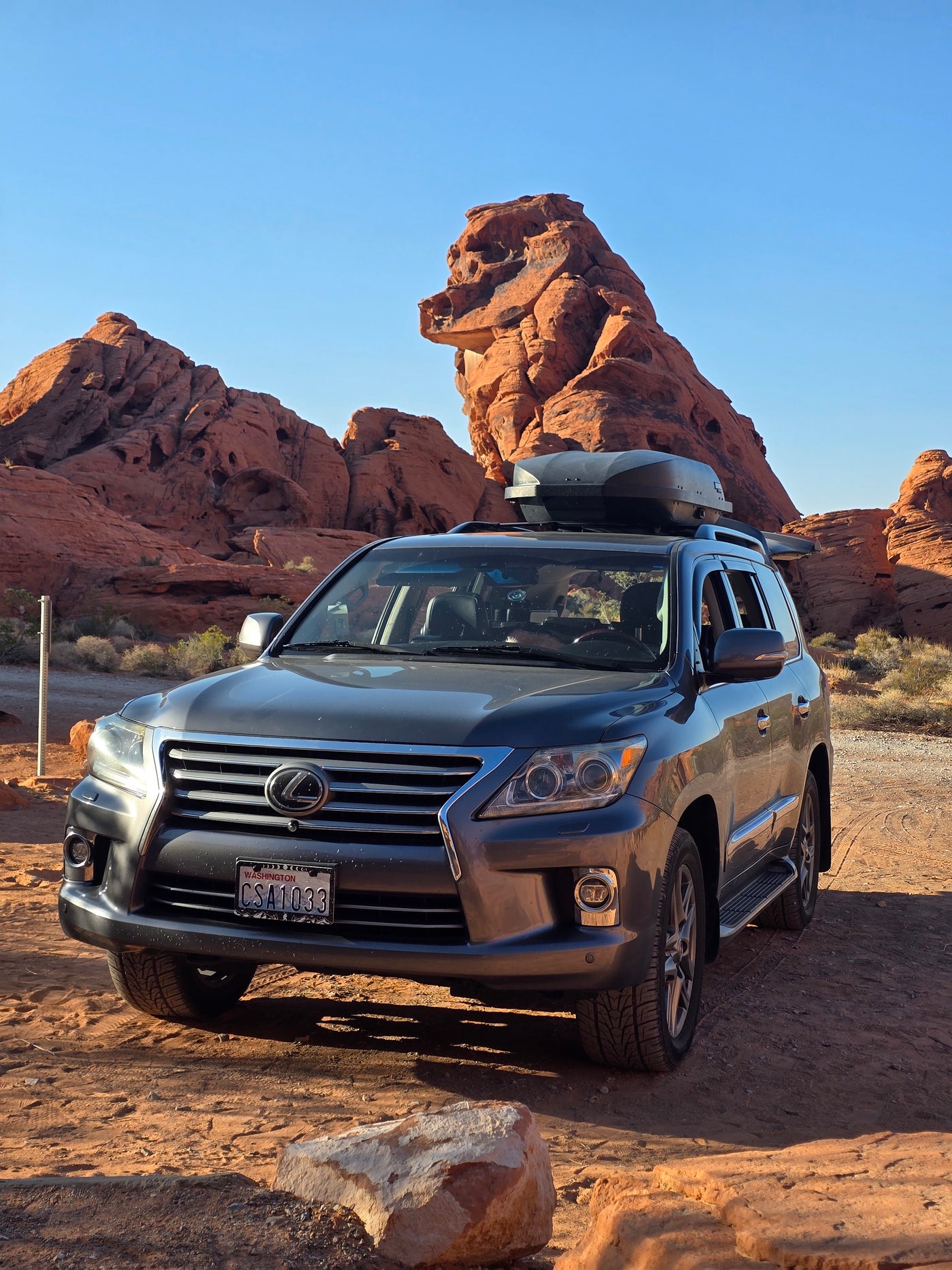 A gray Lexus SUV with a roof cargo box parked amidst striking red rock formations. Ideal for trips where an RV rental is considered. — photo 2