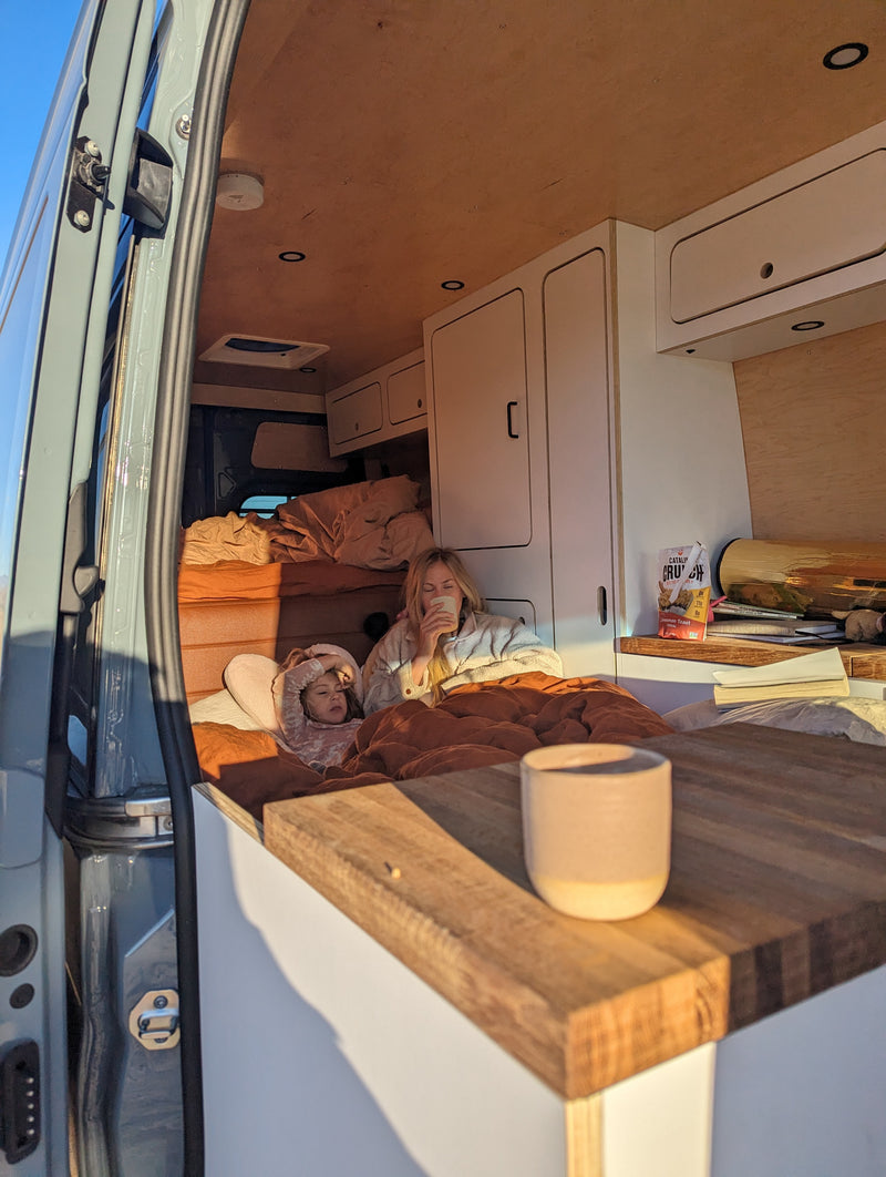 Cozy morning in an RV rental: a woman sips coffee while a child rests in bed inside a custom camper van. Perfect for family adventures. — photo 2