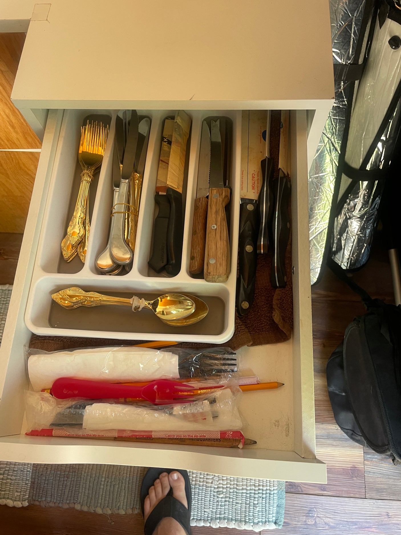 An RV rental kitchen drawer, neatly organized with cutlery, various knives, and everyday items like pencils.