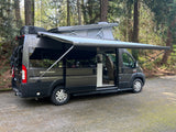 Dark grey pop-top camper van rv rental with extended awning in a wooded setting, perfect for outdoor travel.