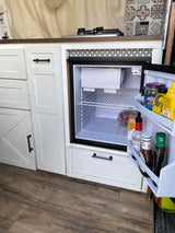 Inside this RV rental: a compact kitchen with an open mini-fridge, small stovetop, and white cabinets. Ready for your adventure!