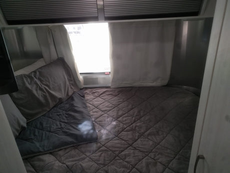 Cozy RV rental bedroom with a plush quilted bed, pillows, and a bright window featuring an "EXIT" sign.