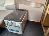 Engel portable fridge/freezer on a textured floor inside an RV rental, with metallic walls & wooden storage.