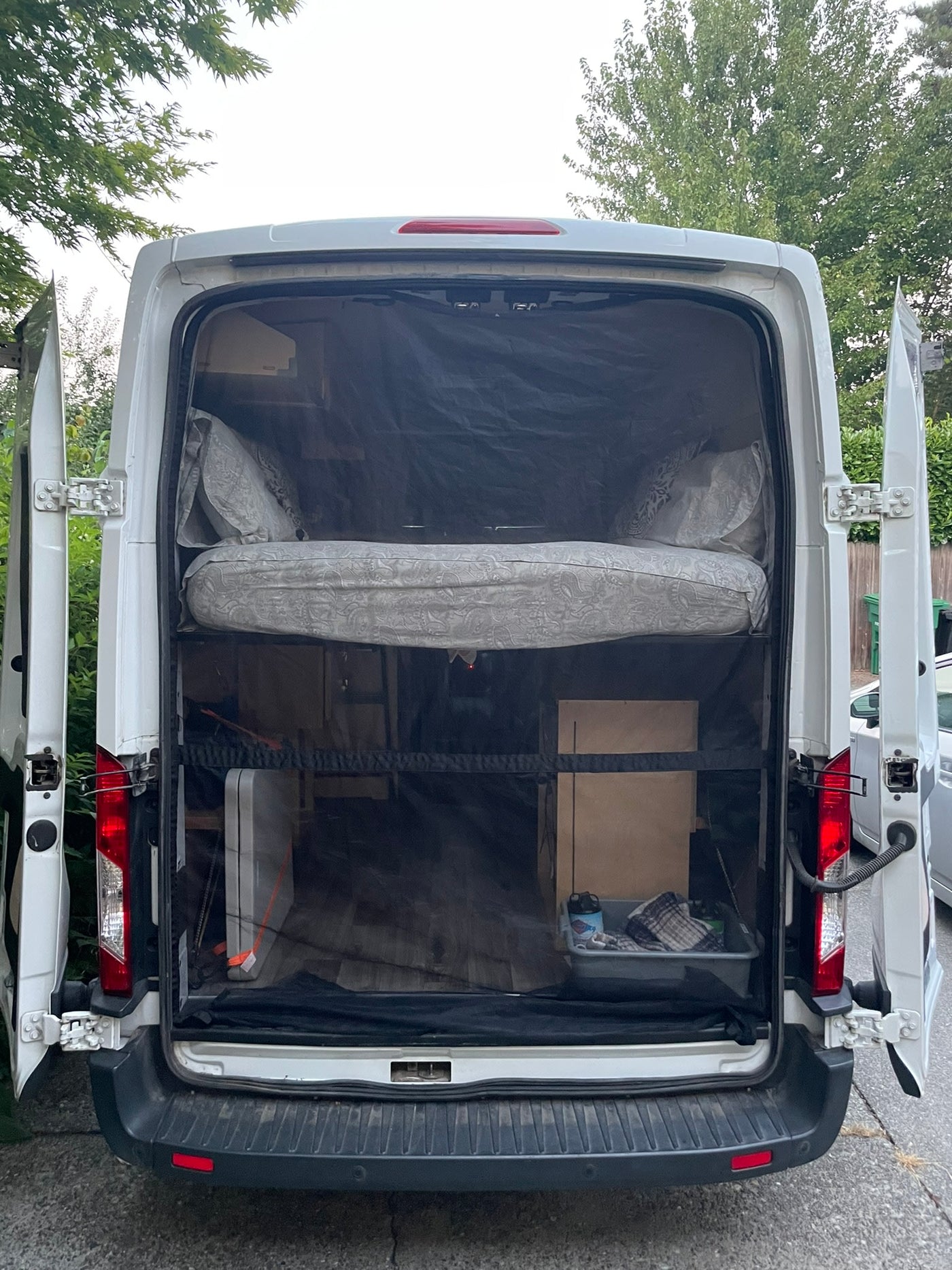 Converted camper van for RV rental, showing its rear with a bed and storage inside, protected by a mesh screen. — photo 18