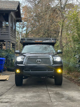 Black Toyota Tundra truck with bright lights & a Four Wheel Pop-Up Camper, ready for rv rental adventures. Parked in a driveway.