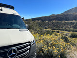 This Mercedes-Benz rv rental is surrounded by vibrant yellow wildflowers and scenic mountains under a clear sky.