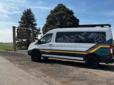 White custom Vandoit rv rental van beside the "Welcome to Colorful Colorado" sign.