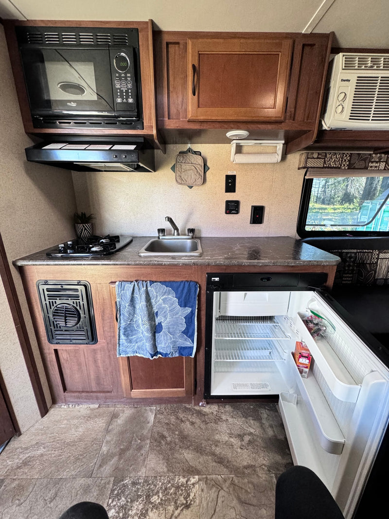 This rv rental's compact kitchen features a microwave, two-burner stove, sink, and open fridge, all neatly arranged. — photo 4