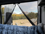 Cozy RV rental bed view through bug screens to majestic mountains and serene forest. Perfect for outdoor escape.