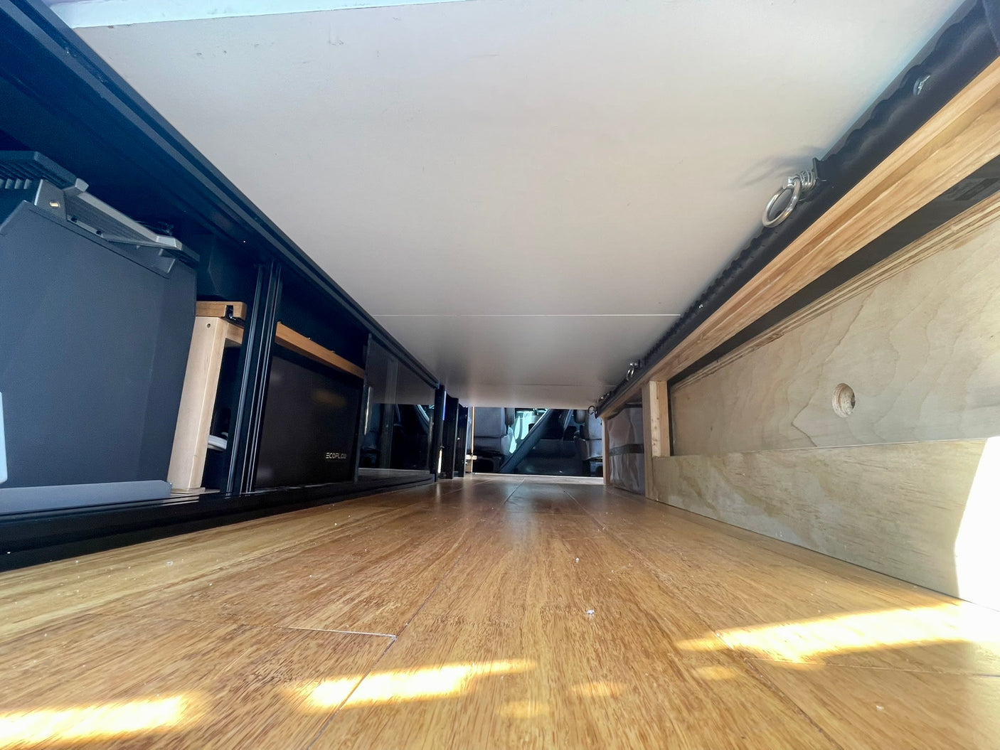 RV rental under-bed storage: ECOFLOW electronics, wood floor, custom cabinetry, and tie-down rails visible.