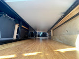 RV rental under-bed storage: ECOFLOW electronics, wood floor, custom cabinetry, and tie-down rails visible.