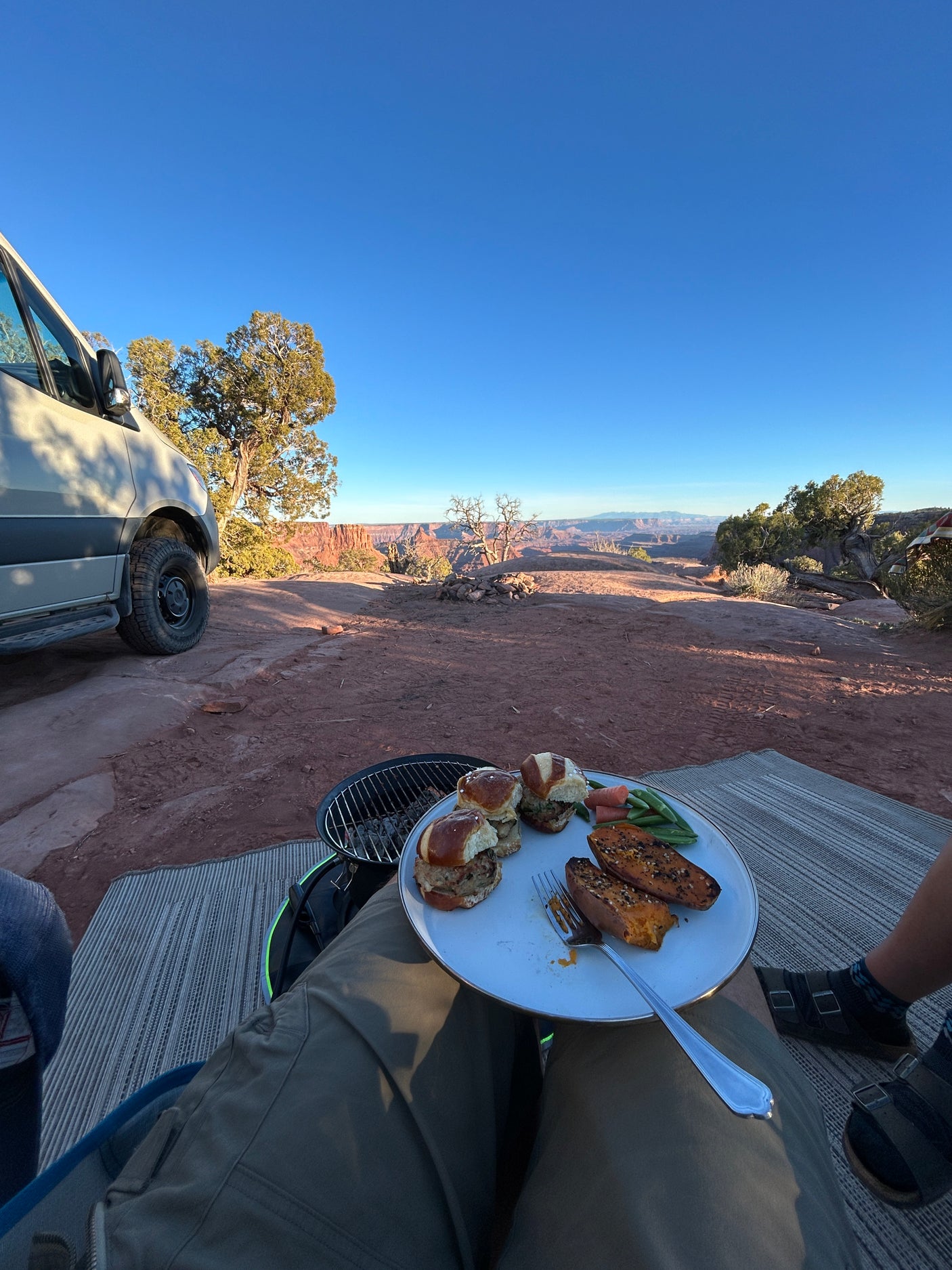 Scenic outdoor dining with an rv rental. Plate of burgers, sweet potatoes, & veggies, overlooking a vast desert canyon landscape.