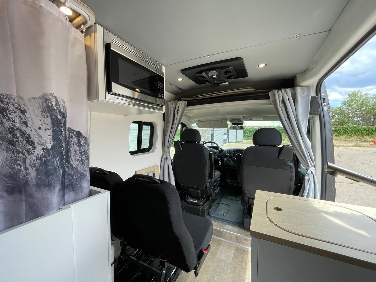 RV rental interior features an overhead microwave, shower curtain with mountain graphic, and front cab view from the living space. — photo 20