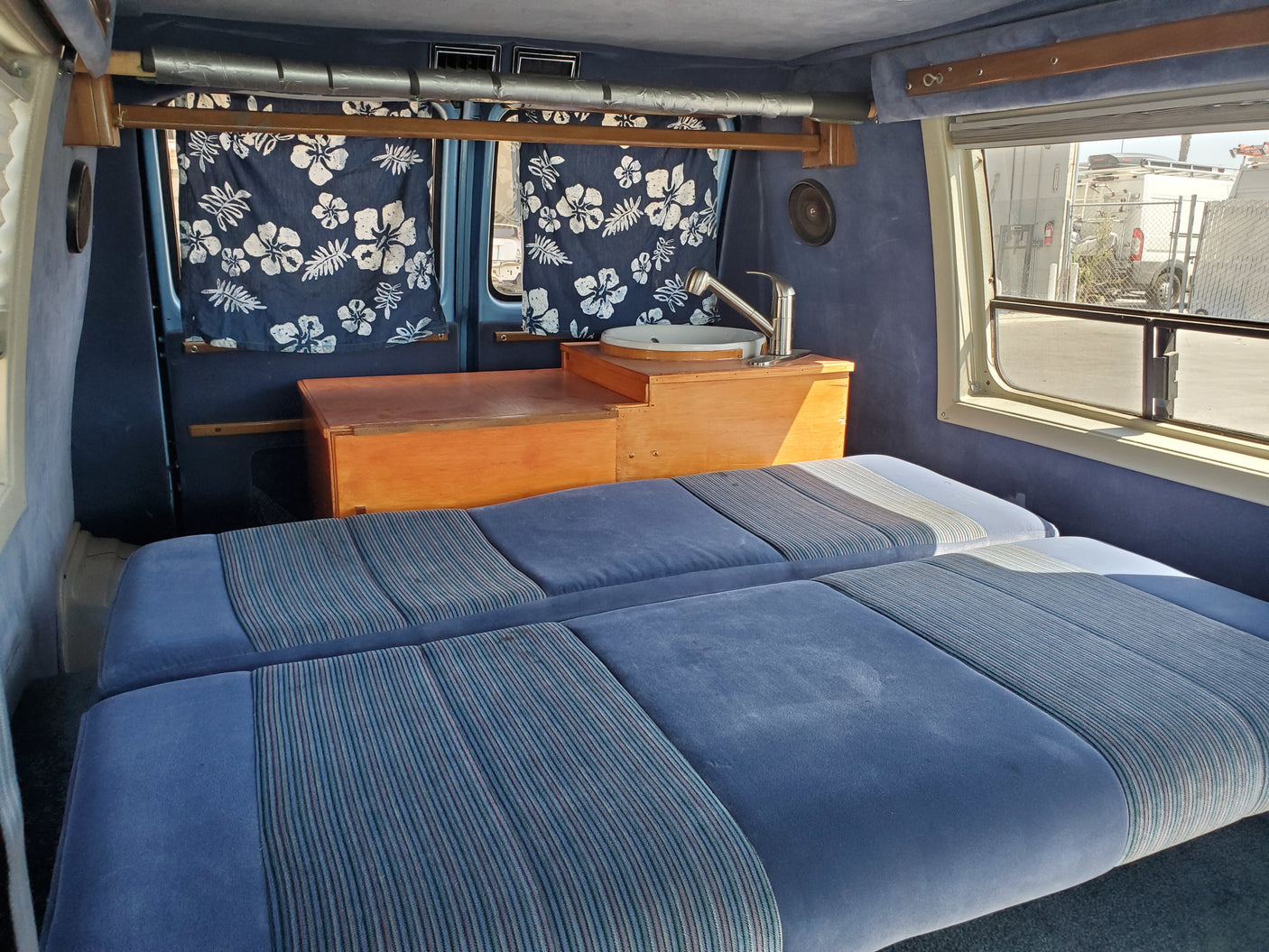 Cozy RV rental interior: blue seating/beds, sink, and flowered curtains. Ready for adventure.