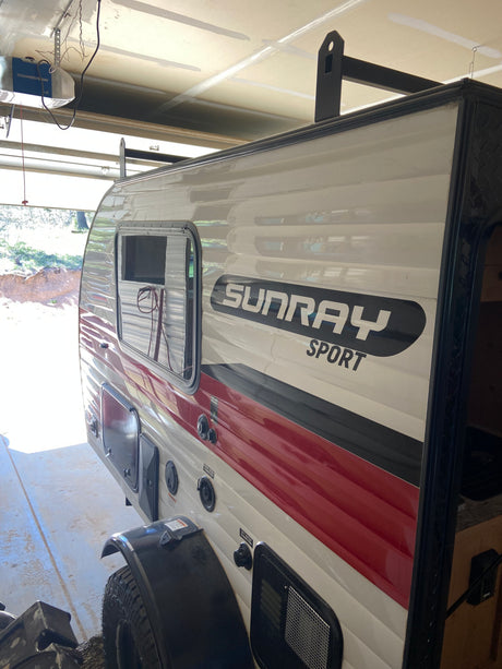 Compact Sunray Sport RV rental parked indoors. The white & red travel trailer's side reveals utility connections.