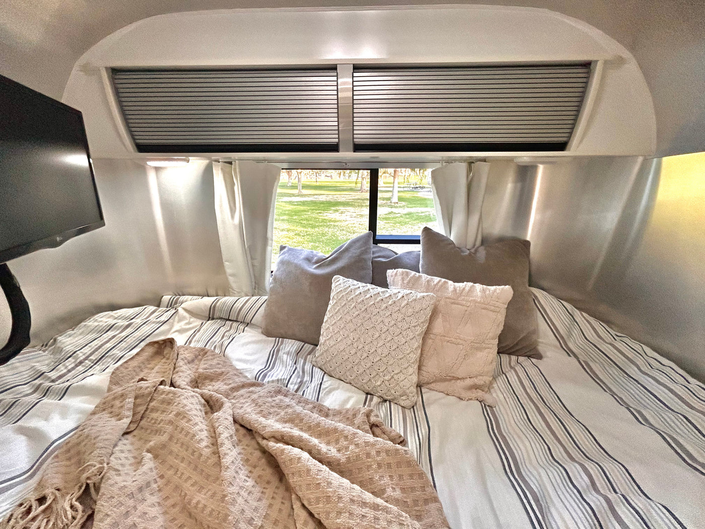 Cozy RV rental bed with striped bedding, various pillows, and a blanket, offering a relaxing view of nature. — photo 10