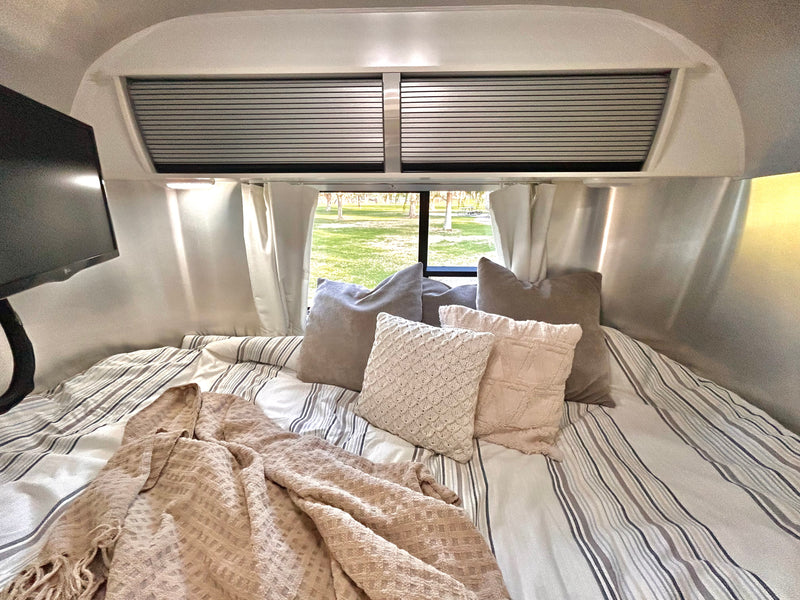 Cozy RV rental bed with striped bedding, various pillows, and a blanket, offering a relaxing view of nature. — photo 10
