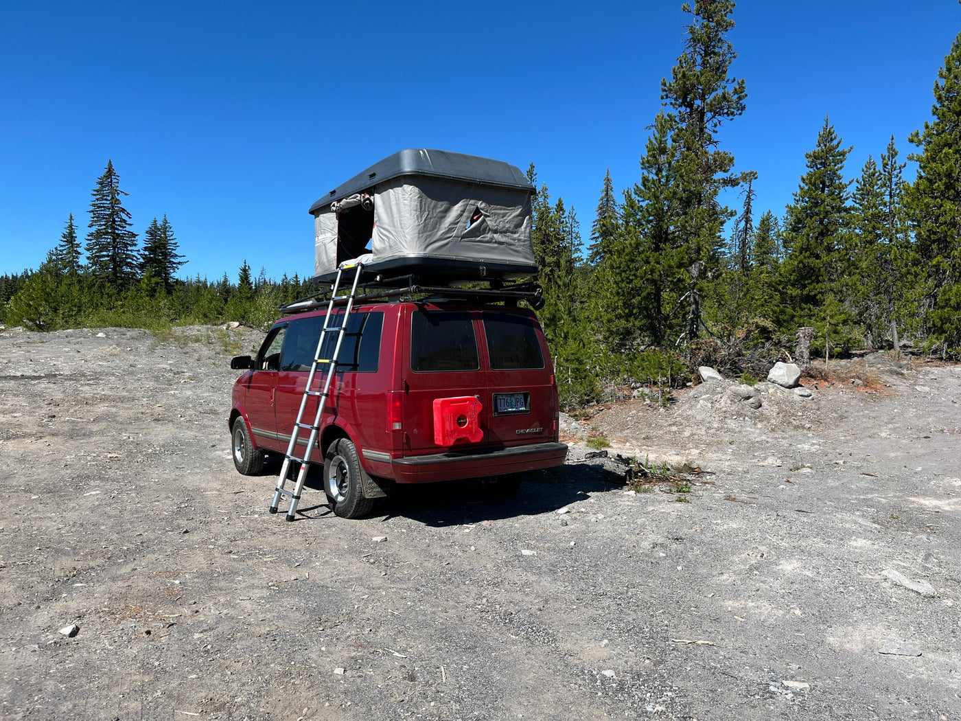 Red RV rental camper van with a rooftop tent and ladder, parked on a sunny gravel path in a forest. — photo 5
