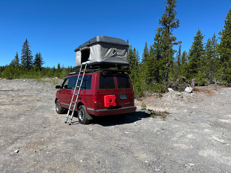 Red RV rental camper van with a rooftop tent and ladder, parked on a sunny gravel path in a forest. — photo 5
