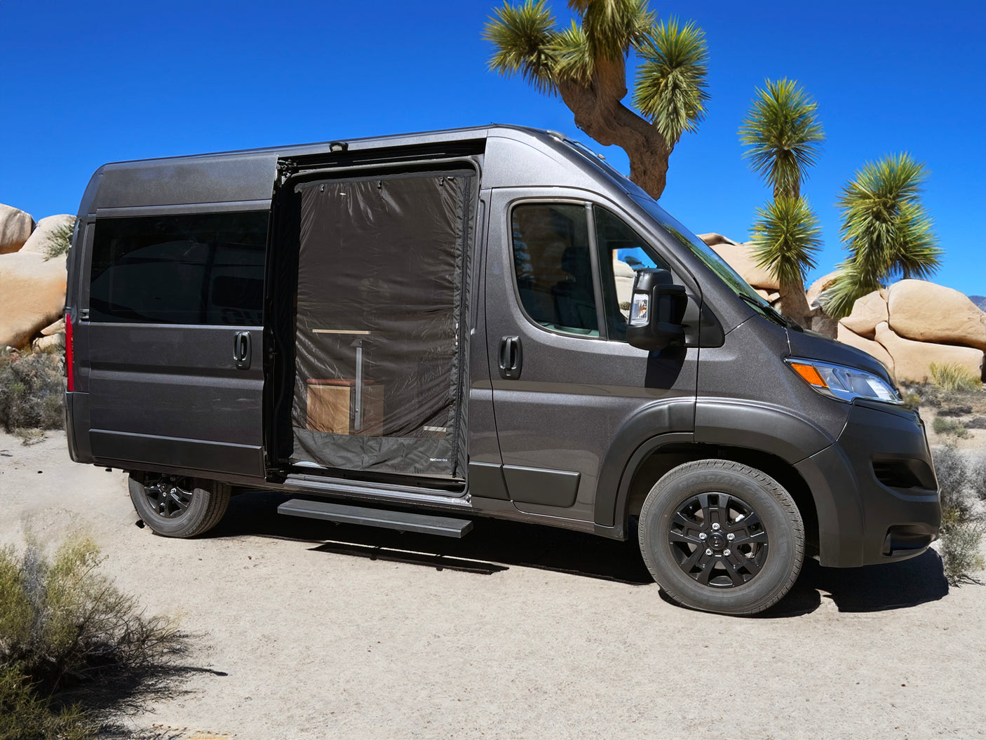 Dark gray rv rental campervan with open screened door, revealing interior, parked in a desert landscape with Joshua trees.