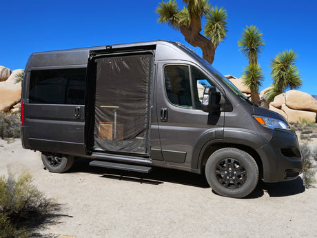 Dark gray rv rental campervan with open screened door, revealing interior, parked in a desert landscape with Joshua trees.