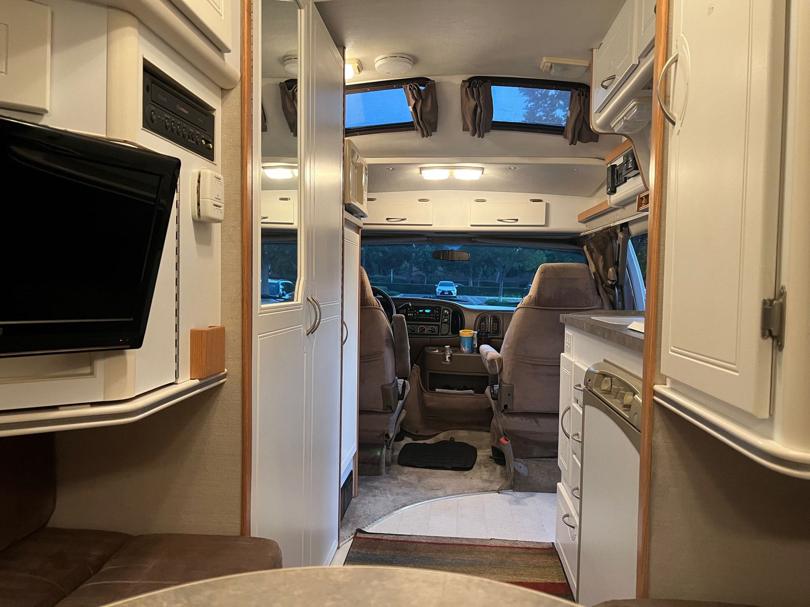 Cozy rv rental interior looking forward from the living area to the driver's cab, showing kitchen, TV, and seating.