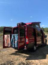 Red Winnebago Solis RV rental parked. Pop-top up, rear doors open with towels. Perfect for outdoor adventures!