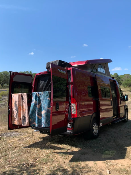 Red Winnebago Solis RV rental parked. Pop-top up, rear doors open with towels. Perfect for outdoor adventures!