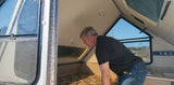 Man leans into an A-frame RV rental, inspecting its light interior. The compact camper features a bed area and numerous windows.