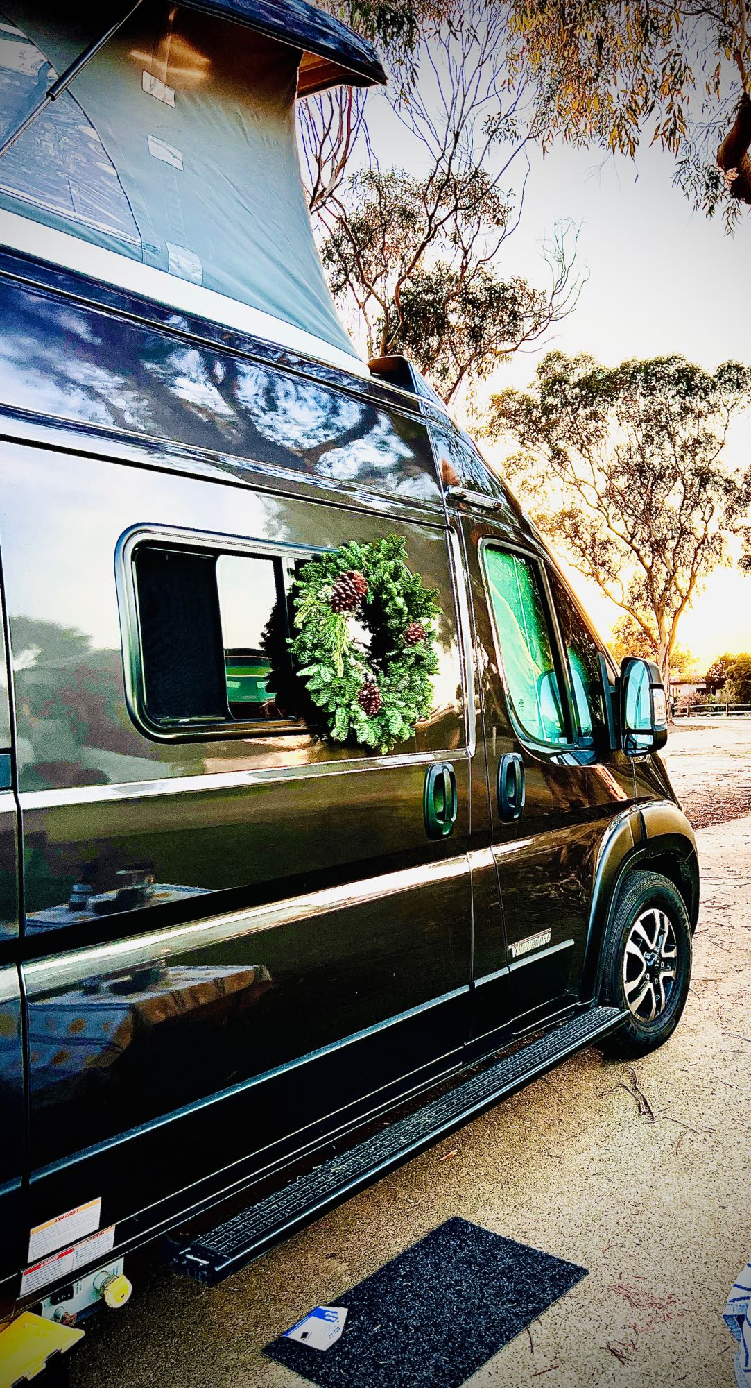 This festive RV rental, a dark camper van with a pop-top and wreath, is set for holiday travel outdoors.