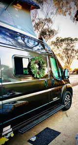 This festive RV rental, a dark camper van with a pop-top and wreath, is set for holiday travel outdoors.