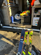 RV rental prepped for skiing. Skis & boots out; camper van interior shows storage, water hookups, and bed.