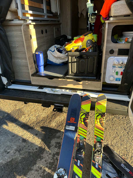 RV rental prepped for skiing. Skis & boots out; camper van interior shows storage, water hookups, and bed.