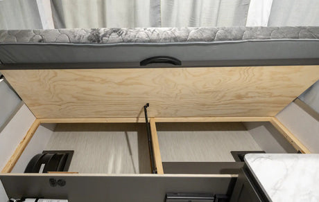 RV rental under-bed storage area, lifted to reveal compartments. Perfect for organizing camping essentials in your travel trailer.