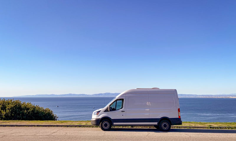  plus a colorful bench and front cab.|White camper van RV rental parked by a stunning ocean view — photo 2