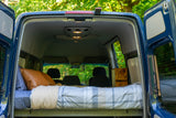 Open rear doors of a blue camper van revealing a comfy bed. Experience van life with this RV rental.
