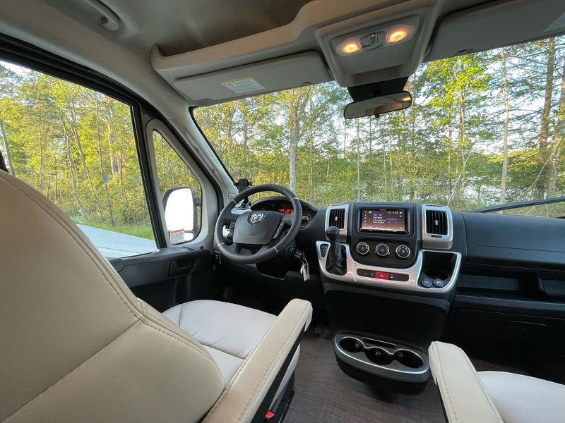 RV rental interior: Driver's seat, steering wheel, and dashboard of a modern RV with trees visible through the windshield. — photo 19