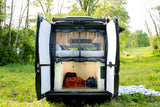 This RV rental's rear doors open to reveal a comfortable bed, storage, and lush green surroundings for your adventure.