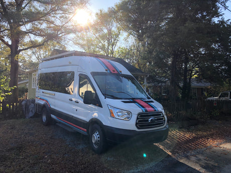White Ford Transit conversion van with bold red/blue stripes & roof rack. Perfect for your next RV rental road trip.