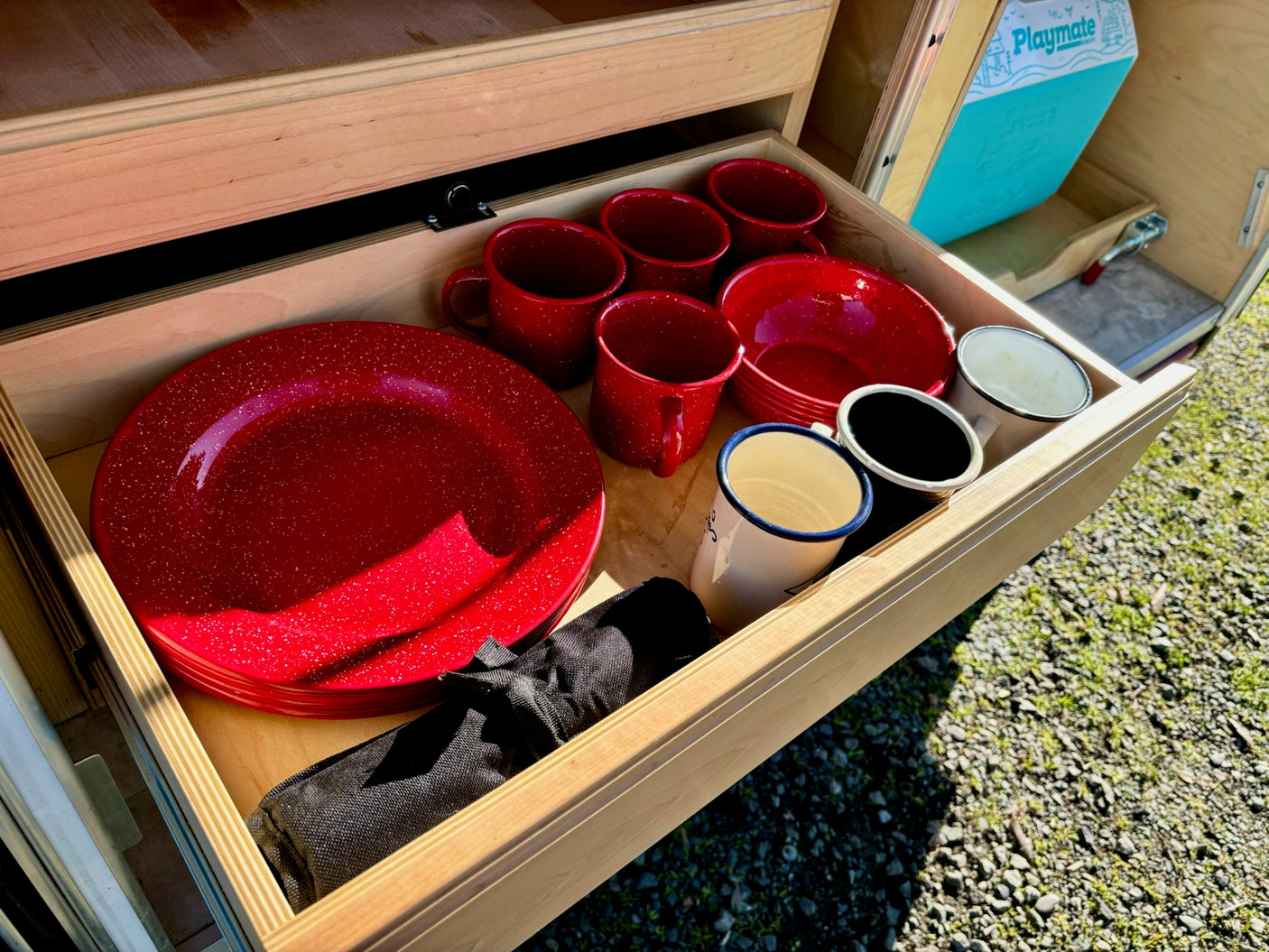 RV rental: A neatly organized wooden drawer holds red speckled enamel plates, bowls, and mugs for camping, plus other cups.