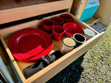 RV rental: A neatly organized wooden drawer holds red speckled enamel plates, bowls, and mugs for camping, plus other cups.