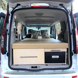 Inside a white RV rental van, a custom bed, storage, & fridge create a cozy camper setup for travel.