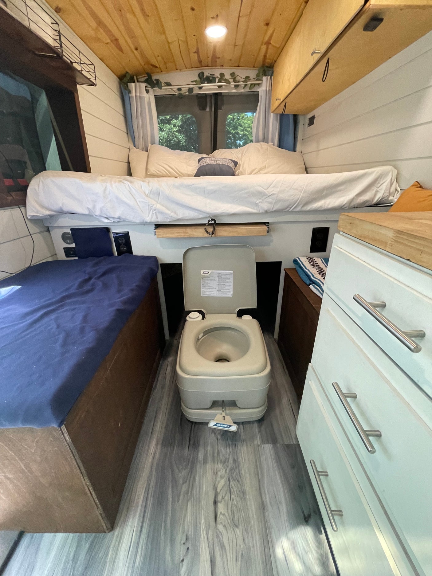 Cozy rv rental interior with a raised bed, portable toilet, and wooden accents, ready for adventure.