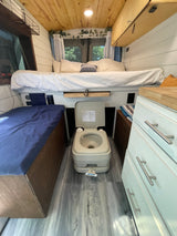 Cozy rv rental interior with a raised bed, portable toilet, and wooden accents, ready for adventure.