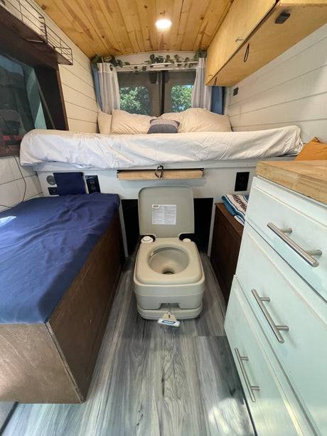 Cozy rv rental interior with a raised bed, portable toilet, and wooden accents, ready for adventure.