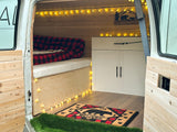 Cozy RV rental interior features wood paneling, string lights, plaid bedding, and bear-themed decor. Ready for adventure!